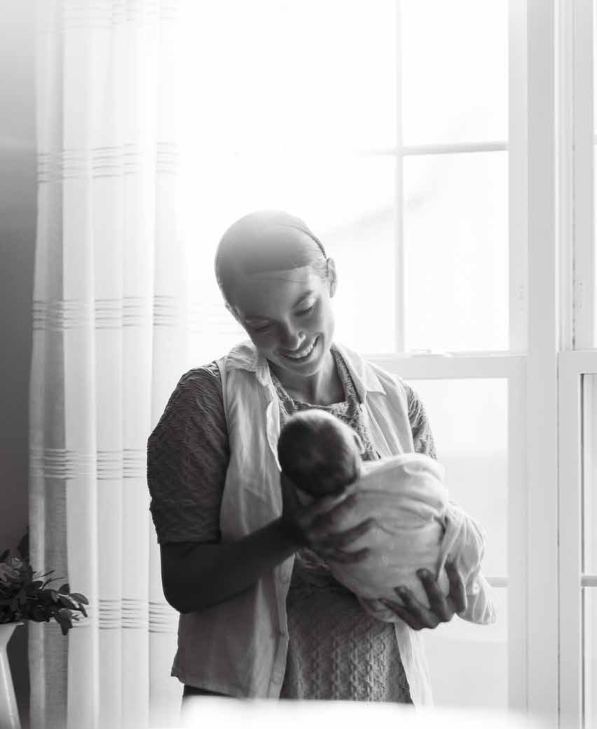 A woman holding an infant beside a bright window