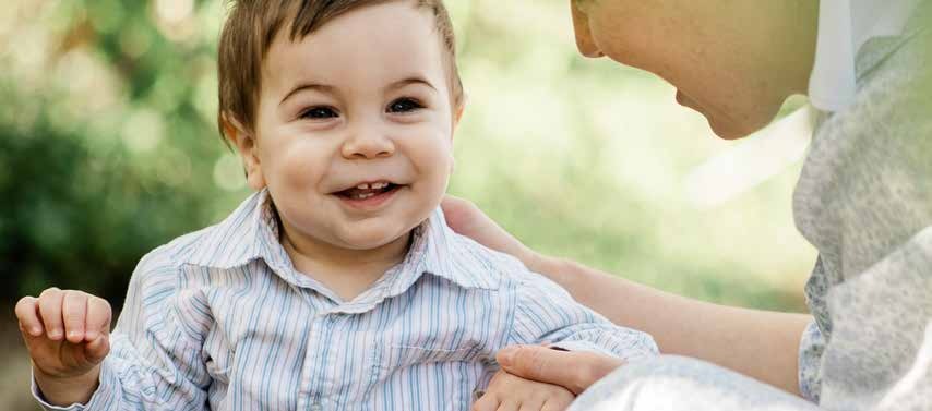 A smiling baby held by an adult outdoors