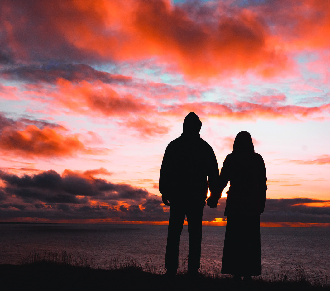 A man and woman holding hands in silhouette against a vivid sunset