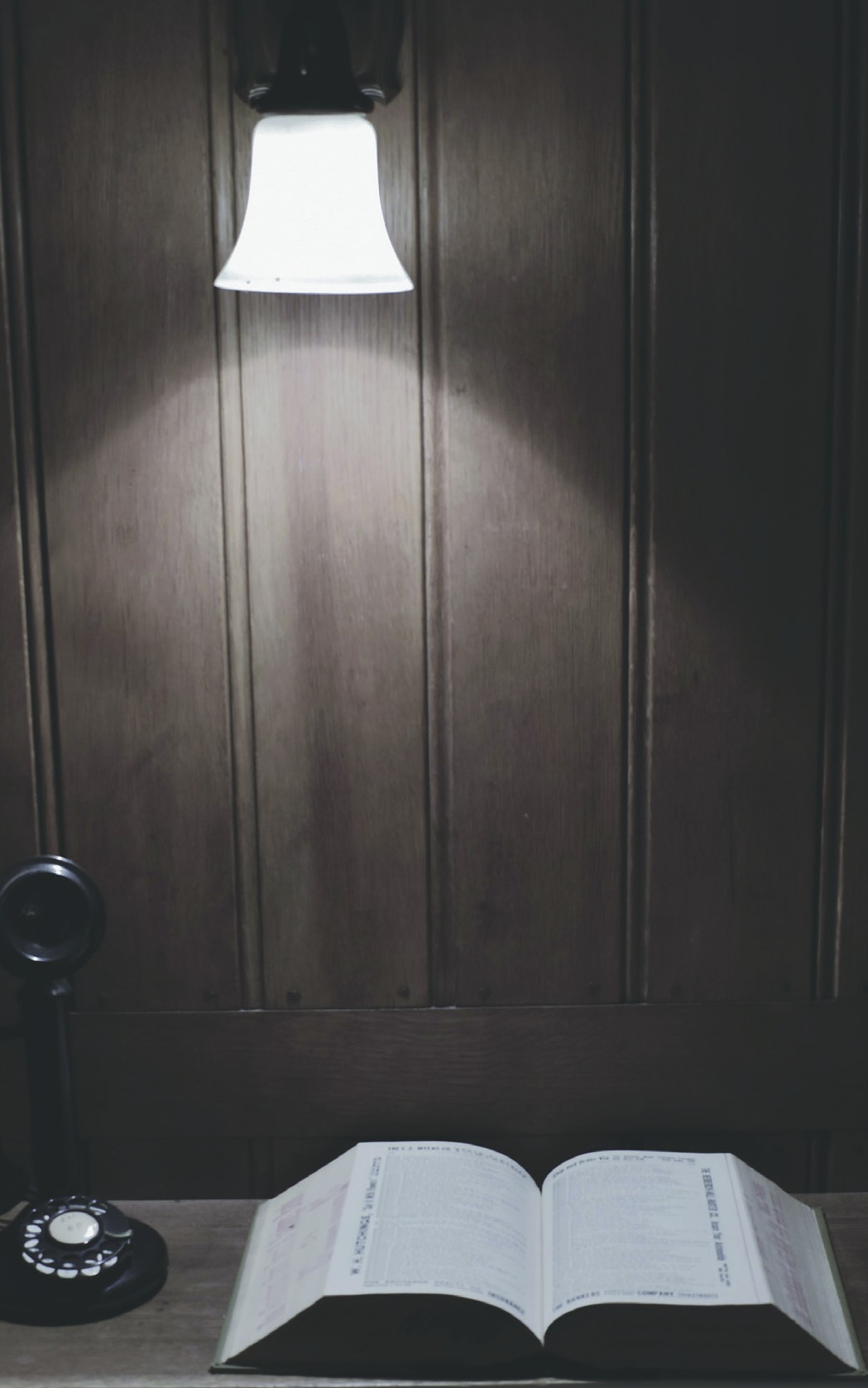 A hanging lamp, wooden door, rotary telephone, and open Bible