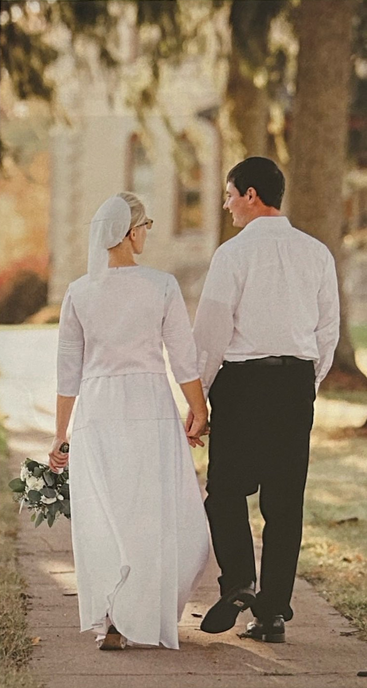 A bride and groom walking hand in hand along a path.