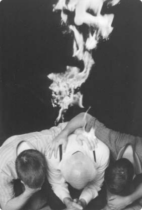 Three men bow together in prayer beneath rising flames.