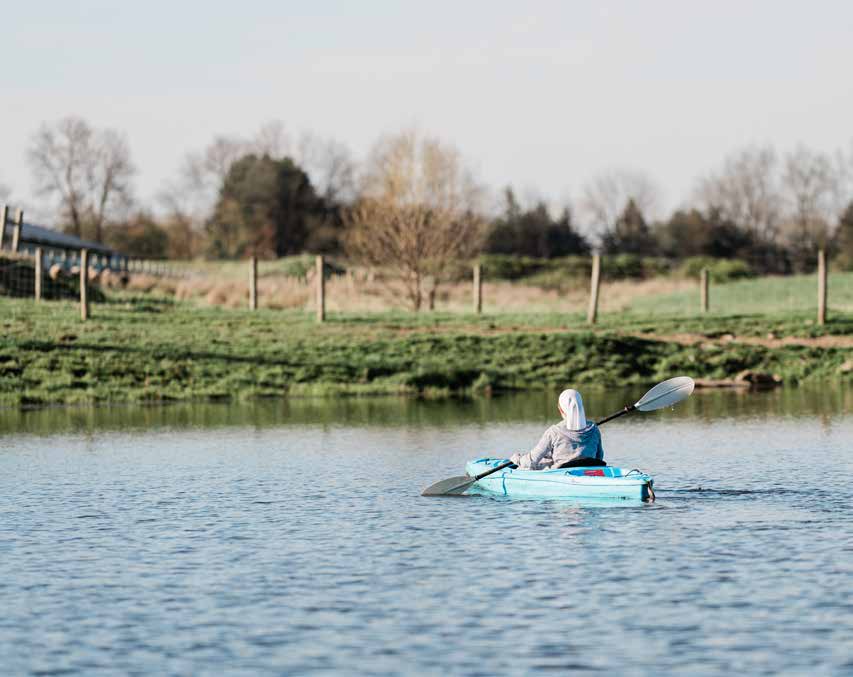 A child paddling a blue kayak on a pond