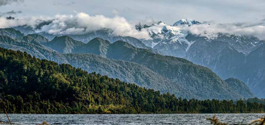 Clouds over snow-capped mountains and a forested lake