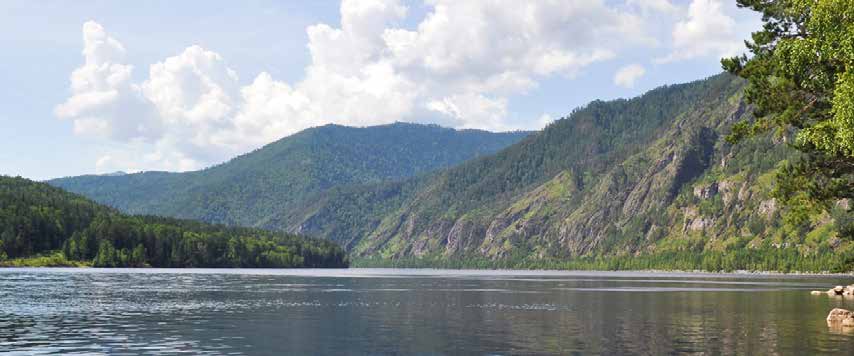 Forested mountains reflected in a lake beneath summer clouds