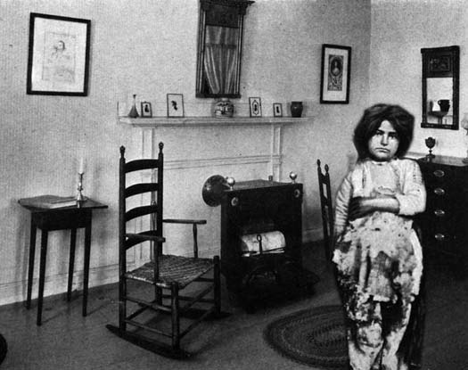 A young girl in ragged clothing standing in a furnished room