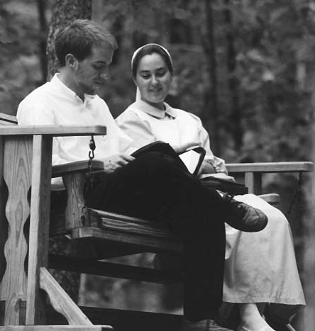A man and woman seated on a wooden bench with open books
