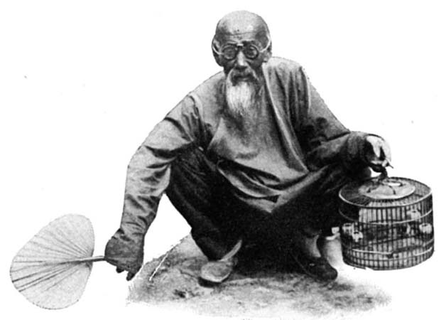An older man holds a fan beside a bird cage