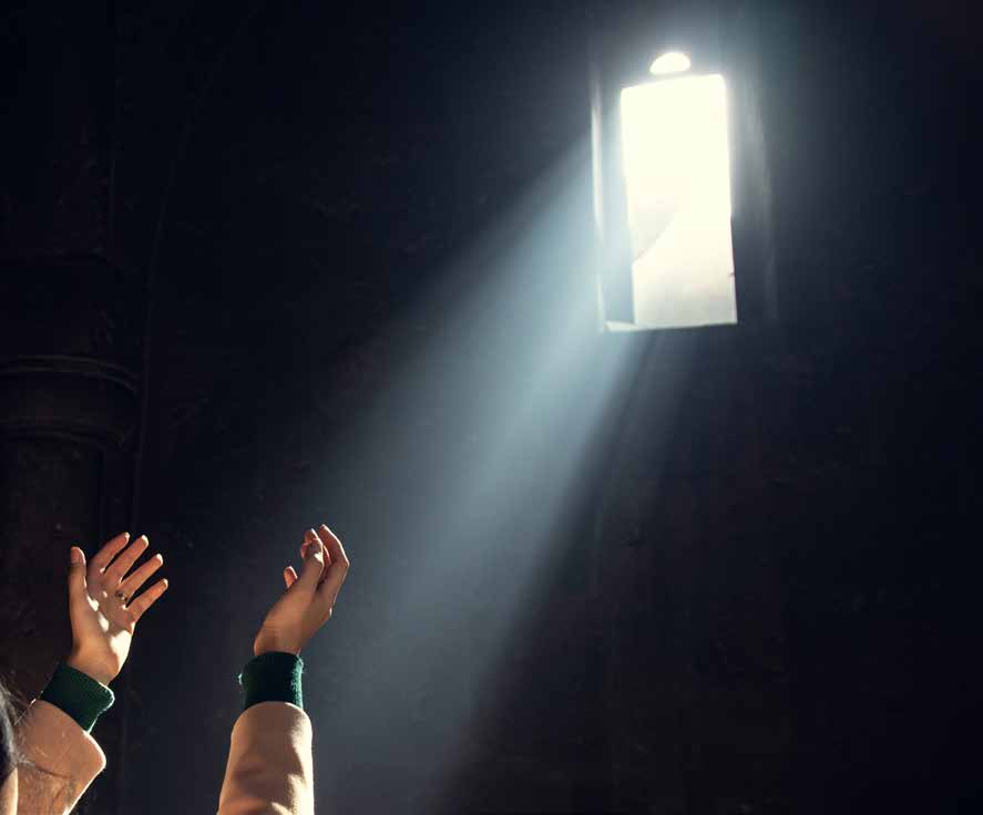 Raised hands reaching toward a beam of light from a high window