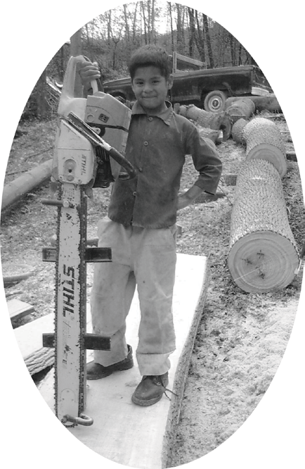 oval photograph of a boy beside a large chainsaw and cut timber
