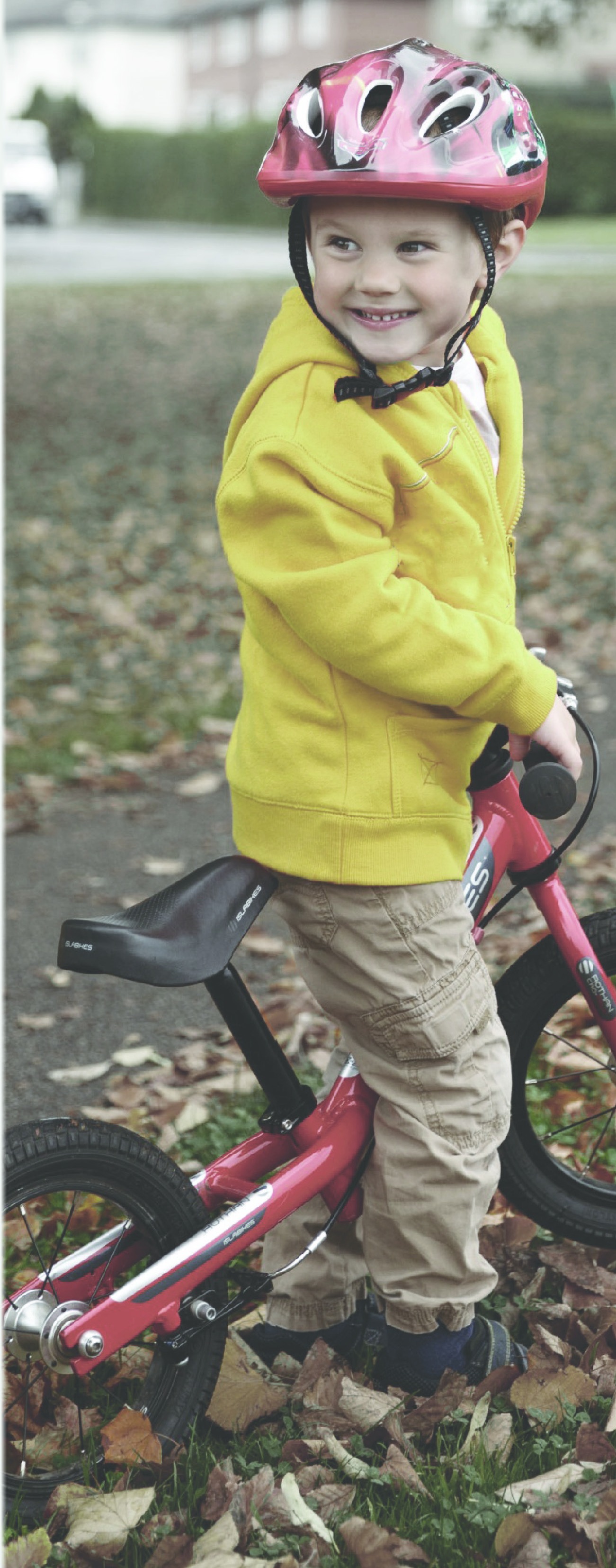 A smiling young boy wearing a helmet and standing with a red bicycle