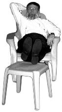 A man reclines with his feet propped on another chair.