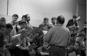 Students gather around a speaker indoors.