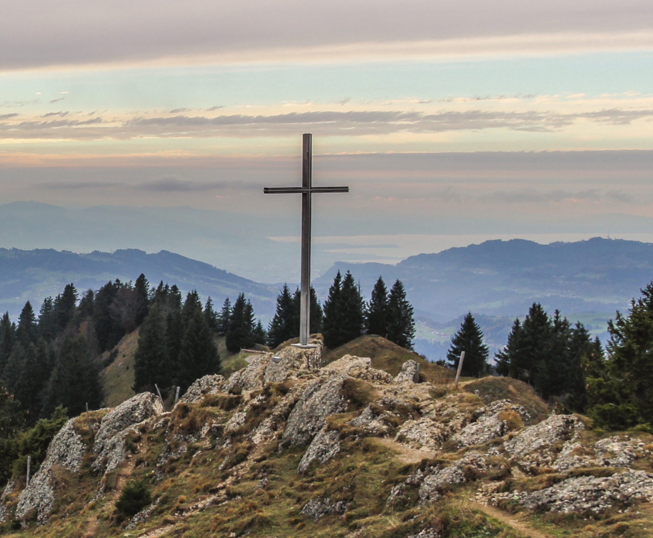 A cross on a rocky mountain overlooking a valley