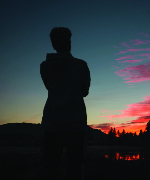 Silhouette of a young person standing beneath a red sunset sky