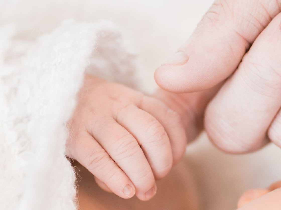 A baby’s hand holding an adult finger