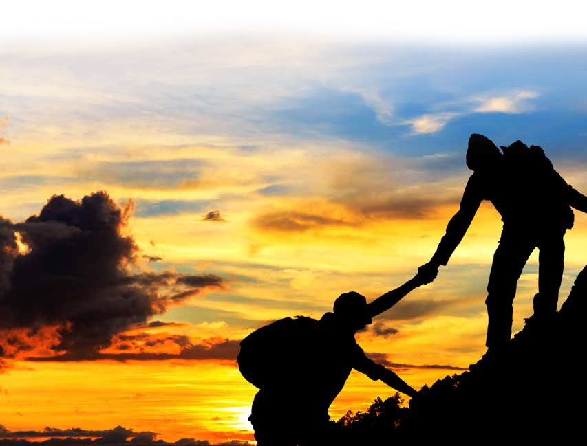 One hiker helping another climb at sunset