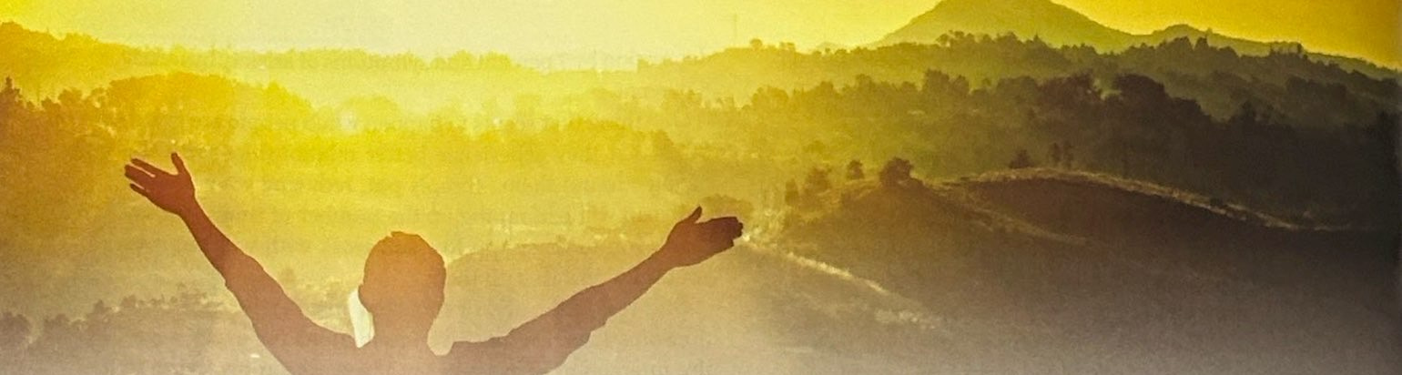 A silhouetted person with raised arms against sunlit hills.