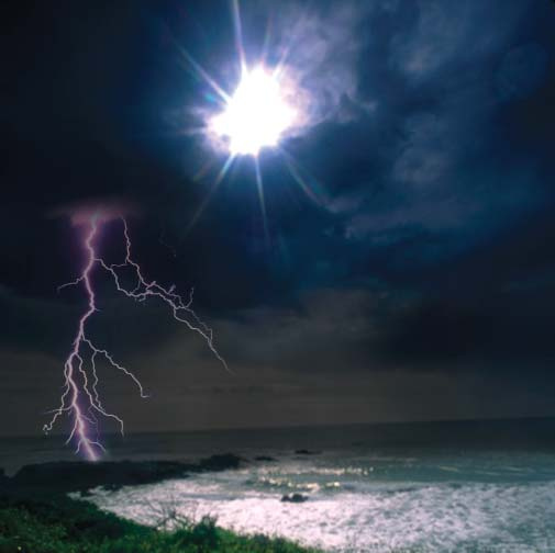 Lightning over a rocky shore beneath a bright light in a dark, clouded sky