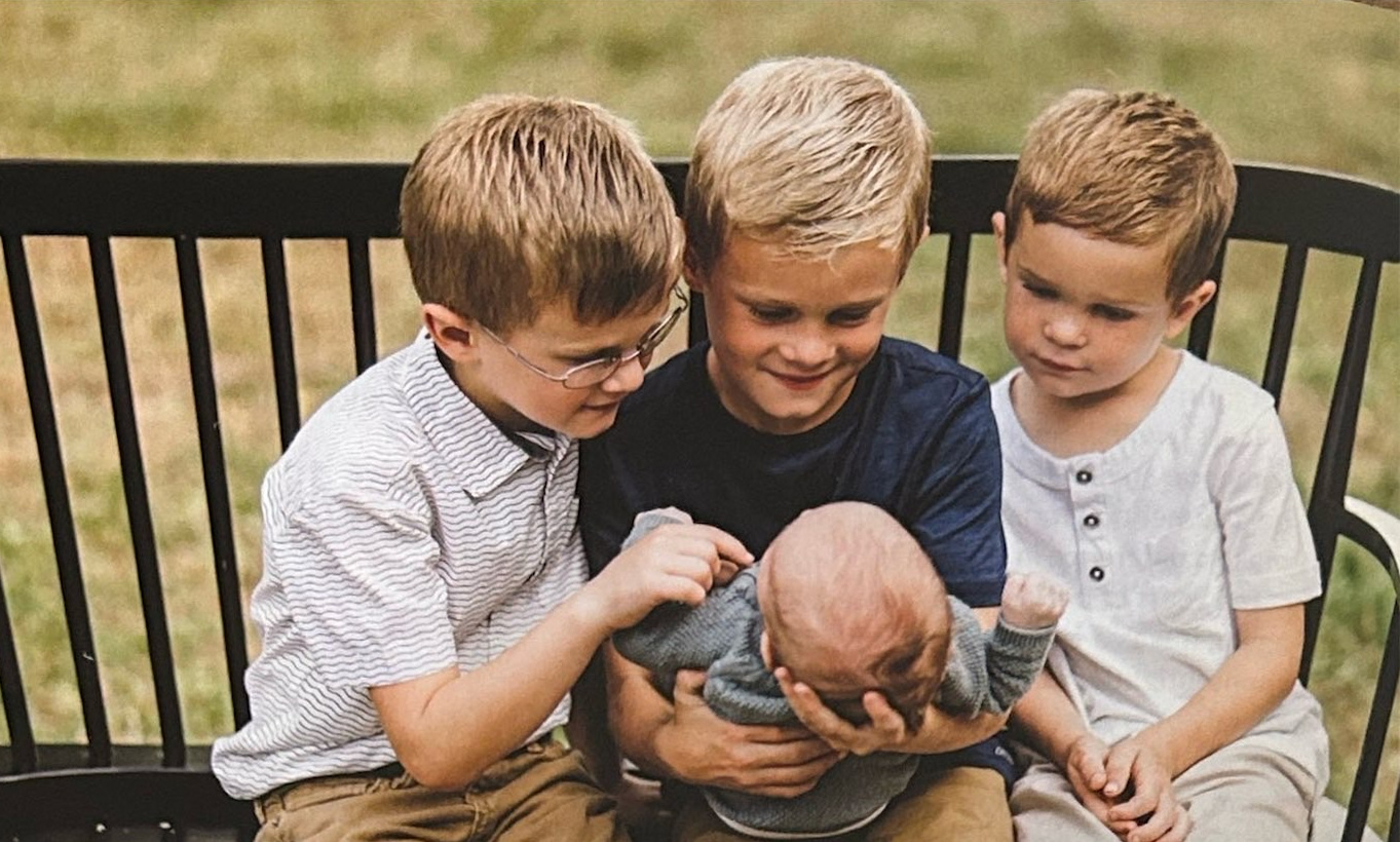 Three boys seated on a bench with a baby.
