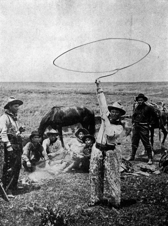 A man twirls a lasso among a group of cowboys and horses.
