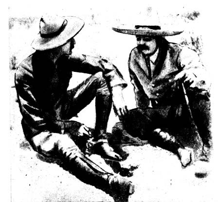 Two men wearing cowboy hats sit on the ground.