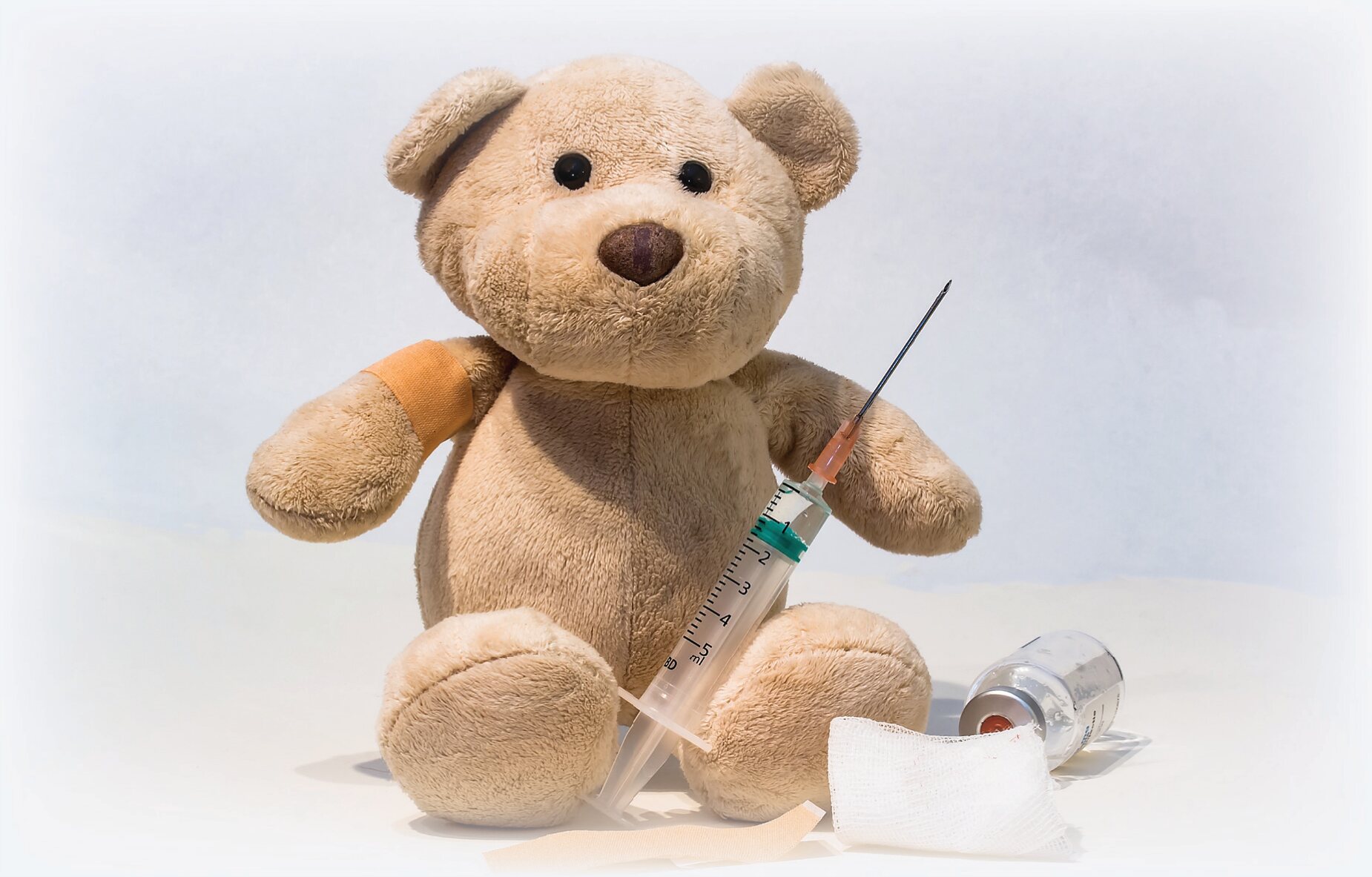 A teddy bear with a syringe, vial, gauze, and adhesive bandage