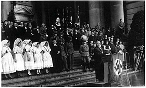A Nazi rally with officials, uniformed girls, and a large crowd