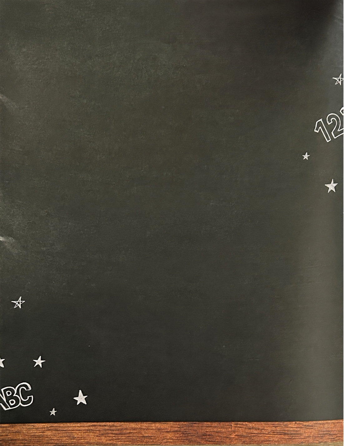 A full chalkboard with chalk stars, letters and numbers around its edges and a wooden ledge along the bottom.