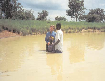 Three people standing in water during a baptism.