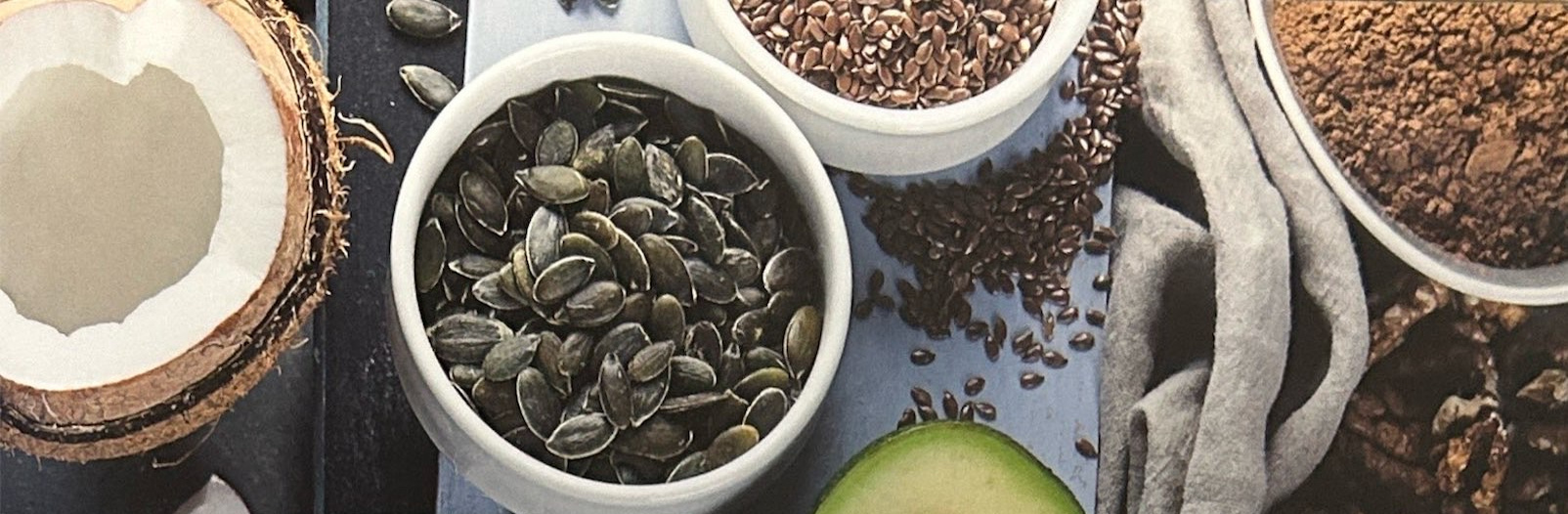 Coconut, seeds, part of an avocado, and bowls of food ingredients.