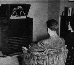 A man seated in a chair watching television