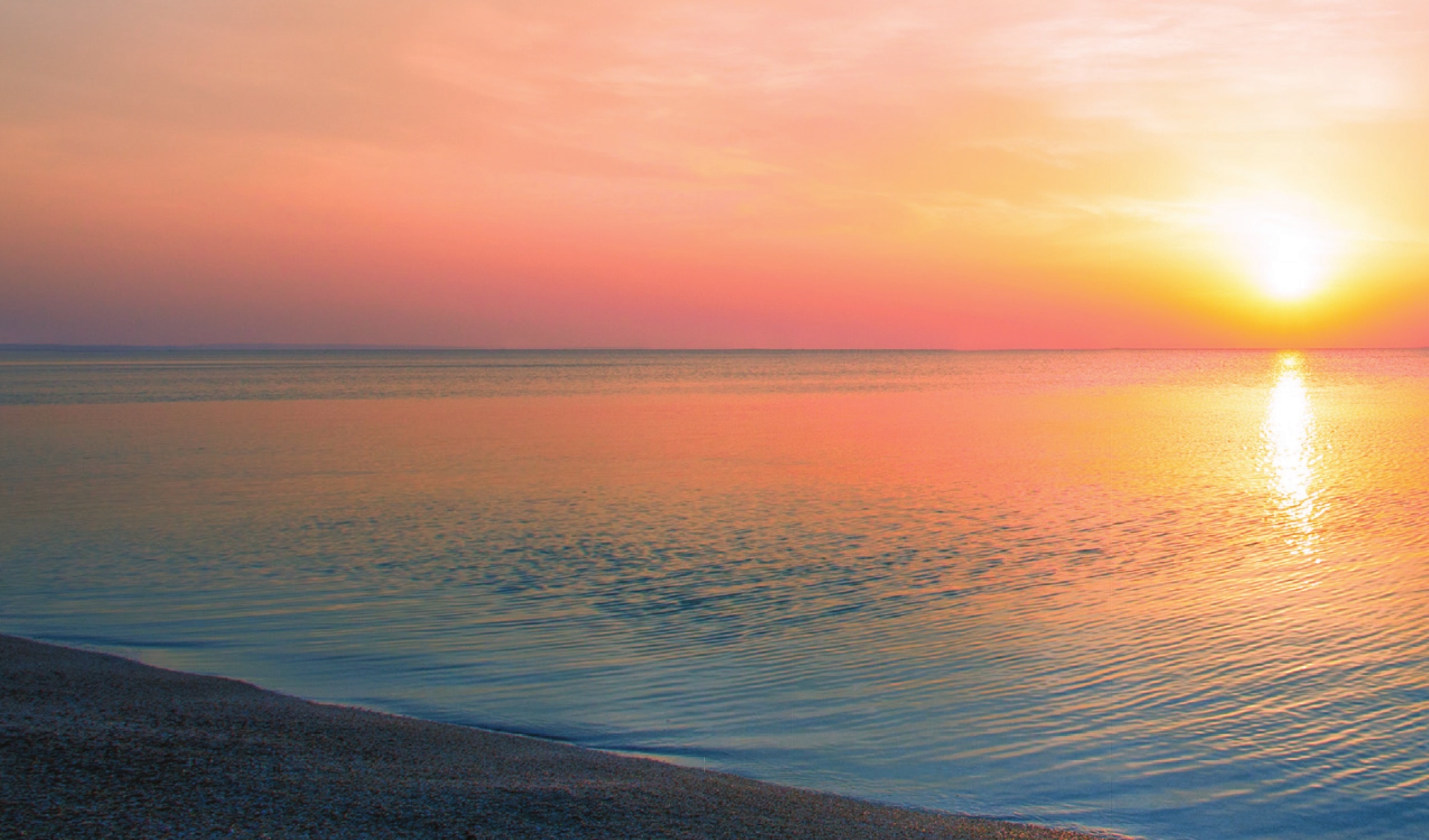 Sunset over calm water and a dark shoreline
