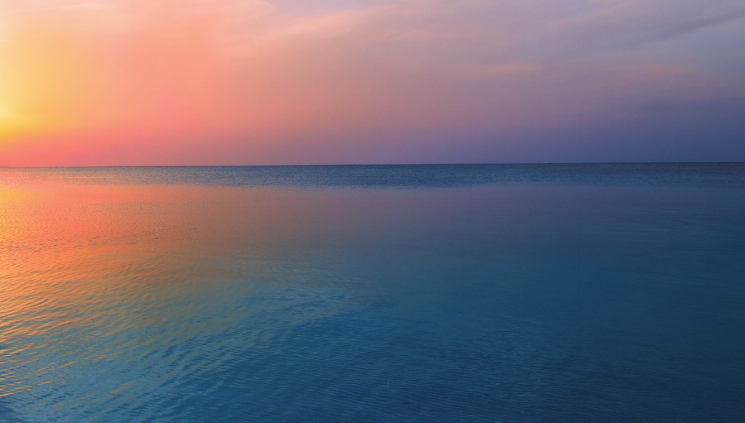 A calm blue sea beneath a pink and orange sky