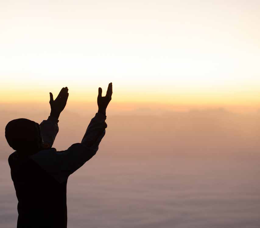 Silhouette of a person raising both hands against a warm sky