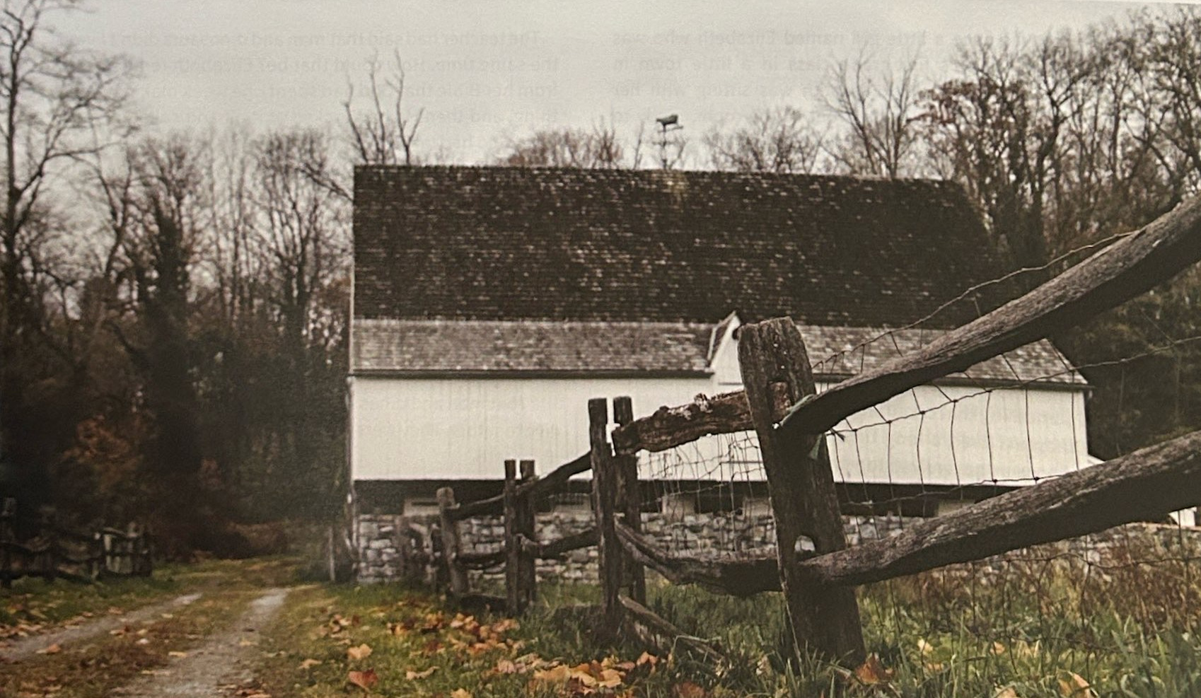 A white barn beyond a wooden fence and a leaf-strewn path.