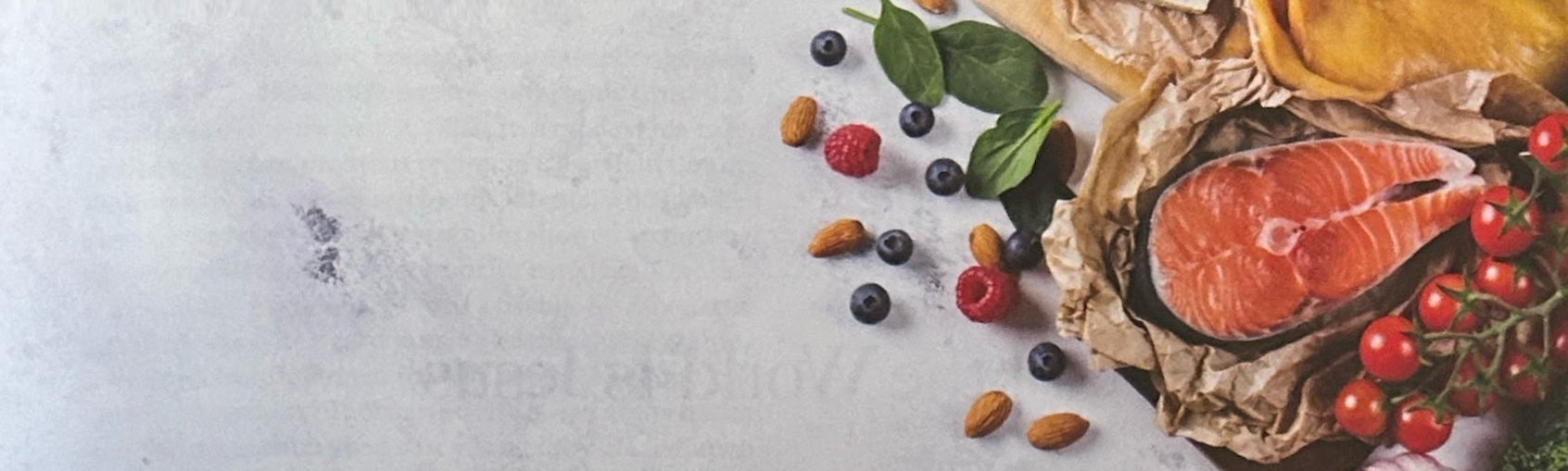 Salmon, berries, nuts, leafy greens and tomatoes on a pale surface.