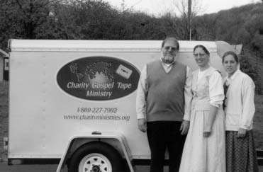 John, Anna, and Mary Joy Weaver stand beside a Tape Ministry trailer.