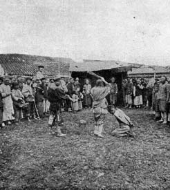 A man raising a sword over a kneeling person as a crowd watches