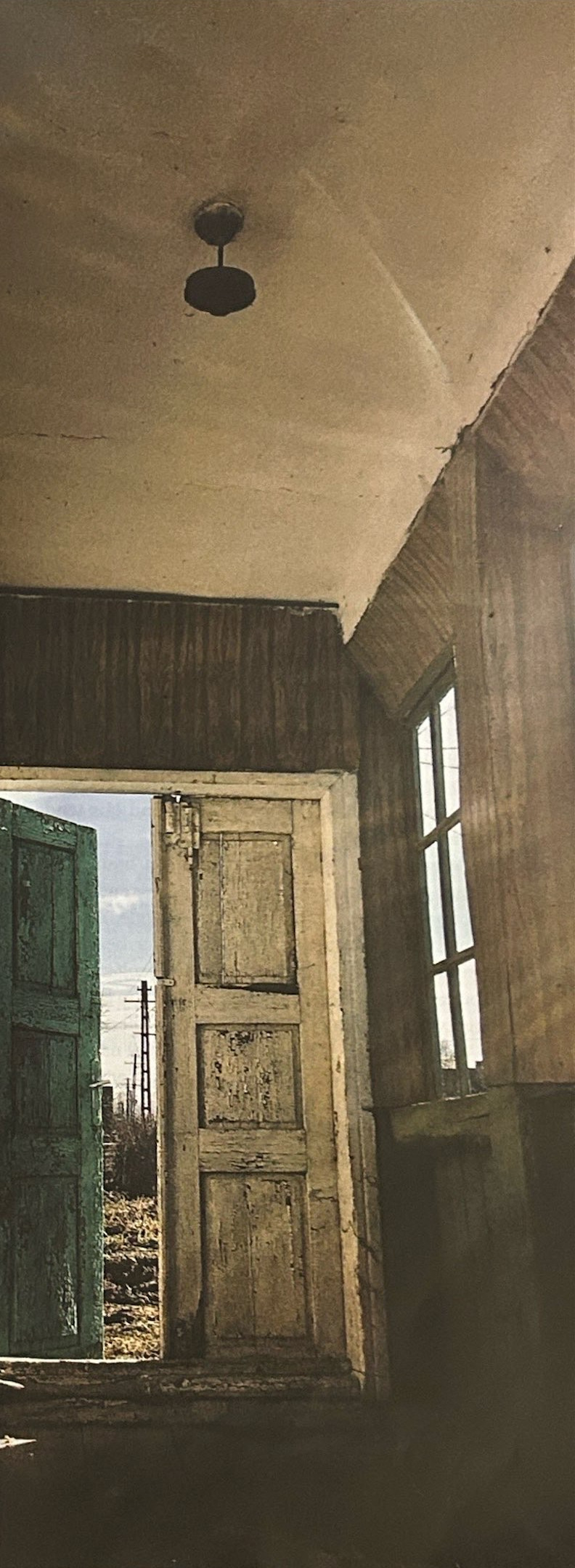 An open weathered doorway and tall window in an empty room.
