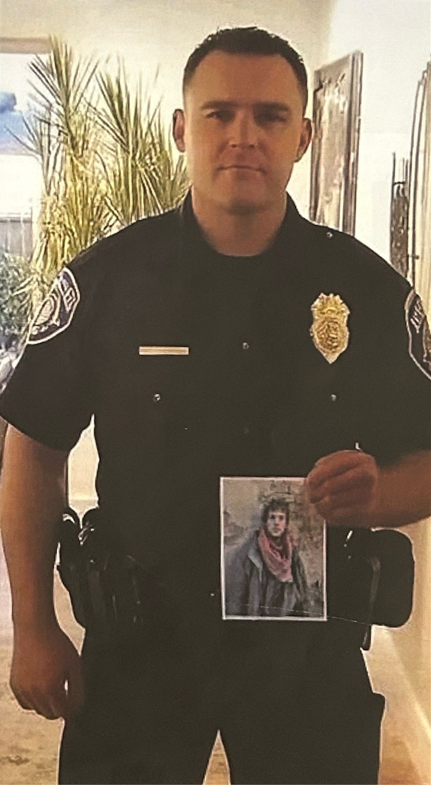 A uniformed police officer holding a photograph of a person wearing a scarf.
