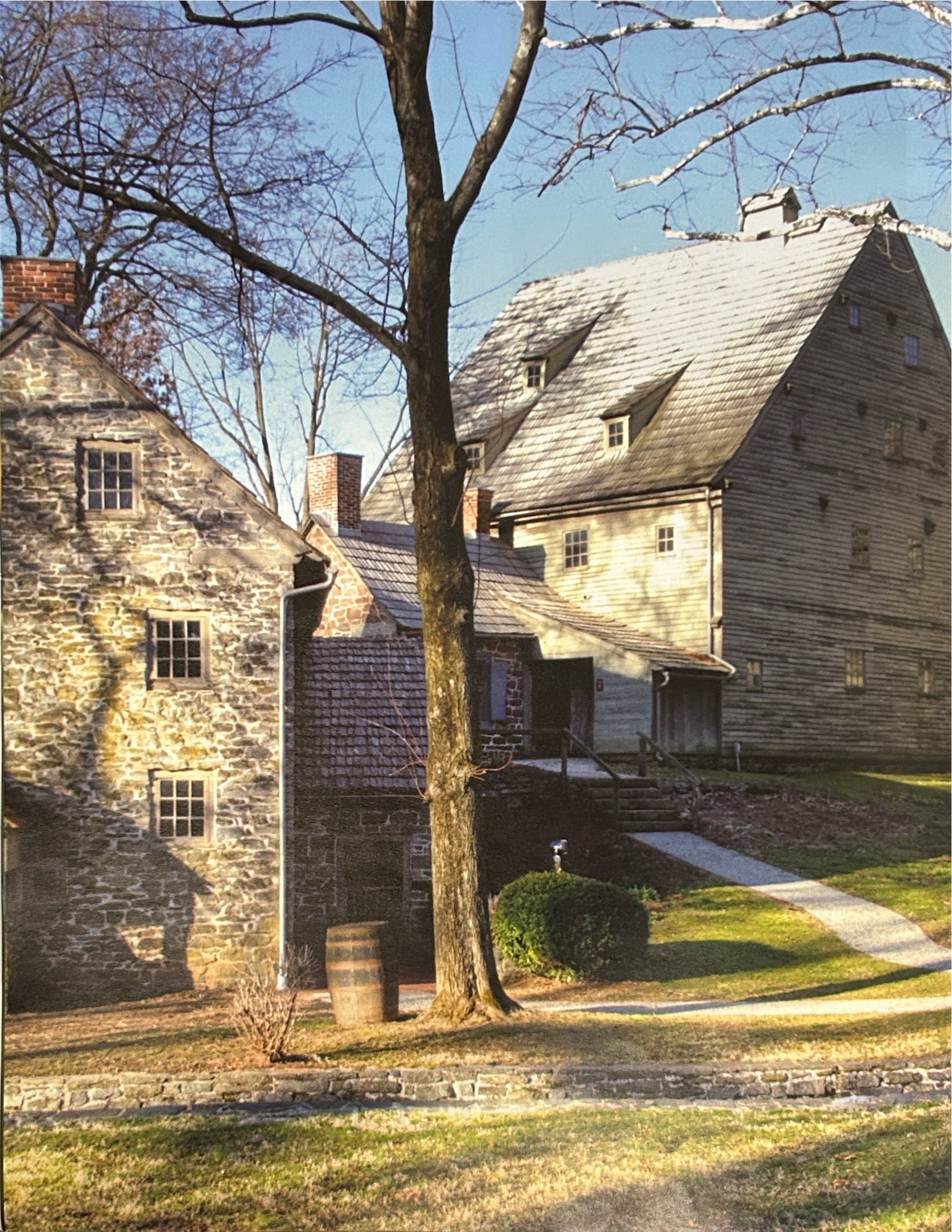 Stone and timber buildings of the Ephrata Cloister with a bare tree and paths in front.