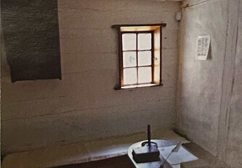 A simple room with a window, a wooden bench and a small table with a candle.