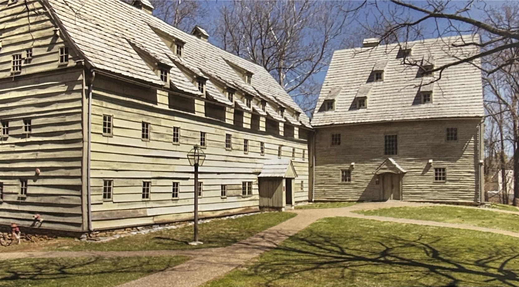 Two timber buildings at the Ephrata Cloister beside a lawn and paths.