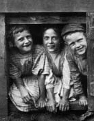 Three smiling children leaning forward in a doorway.