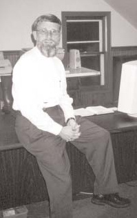 Denny Kenaston seated beside a desk.