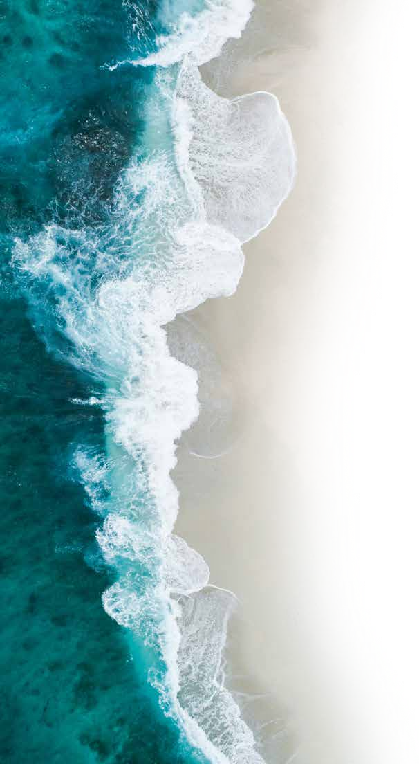 Oseaanwaaiers wat langs ’n sandstrand breek, gesien van bo af.