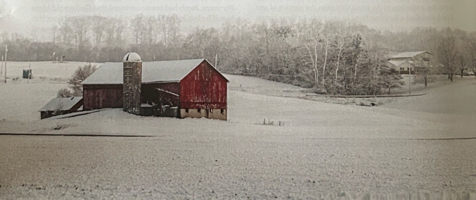 Red barn and silo in a snow-covered field.