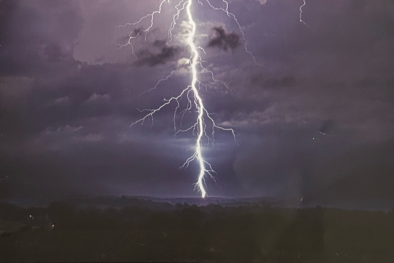 A branching lightning bolt illuminates storm clouds above a dark wooded landscape.