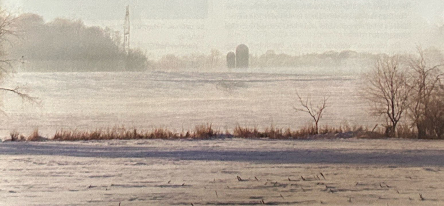 Snow-covered fields with distant silos and bare trees.